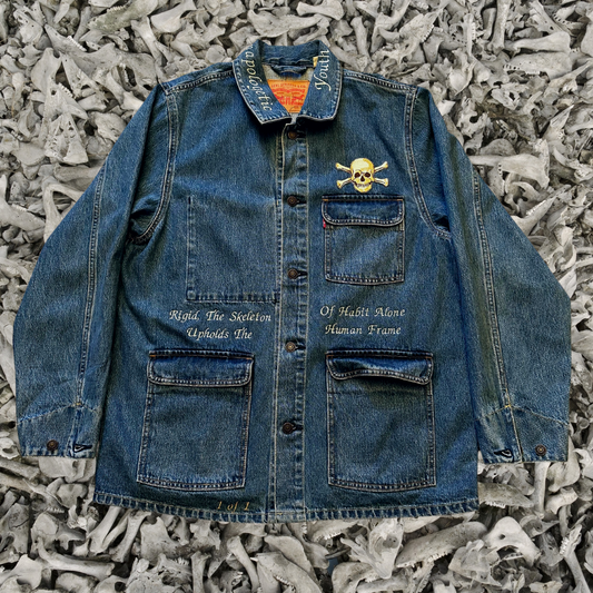 Unapologetic Youth denim jean jacket with bone graphic design, classic fit, and button-front closure, displayed on a hanger.