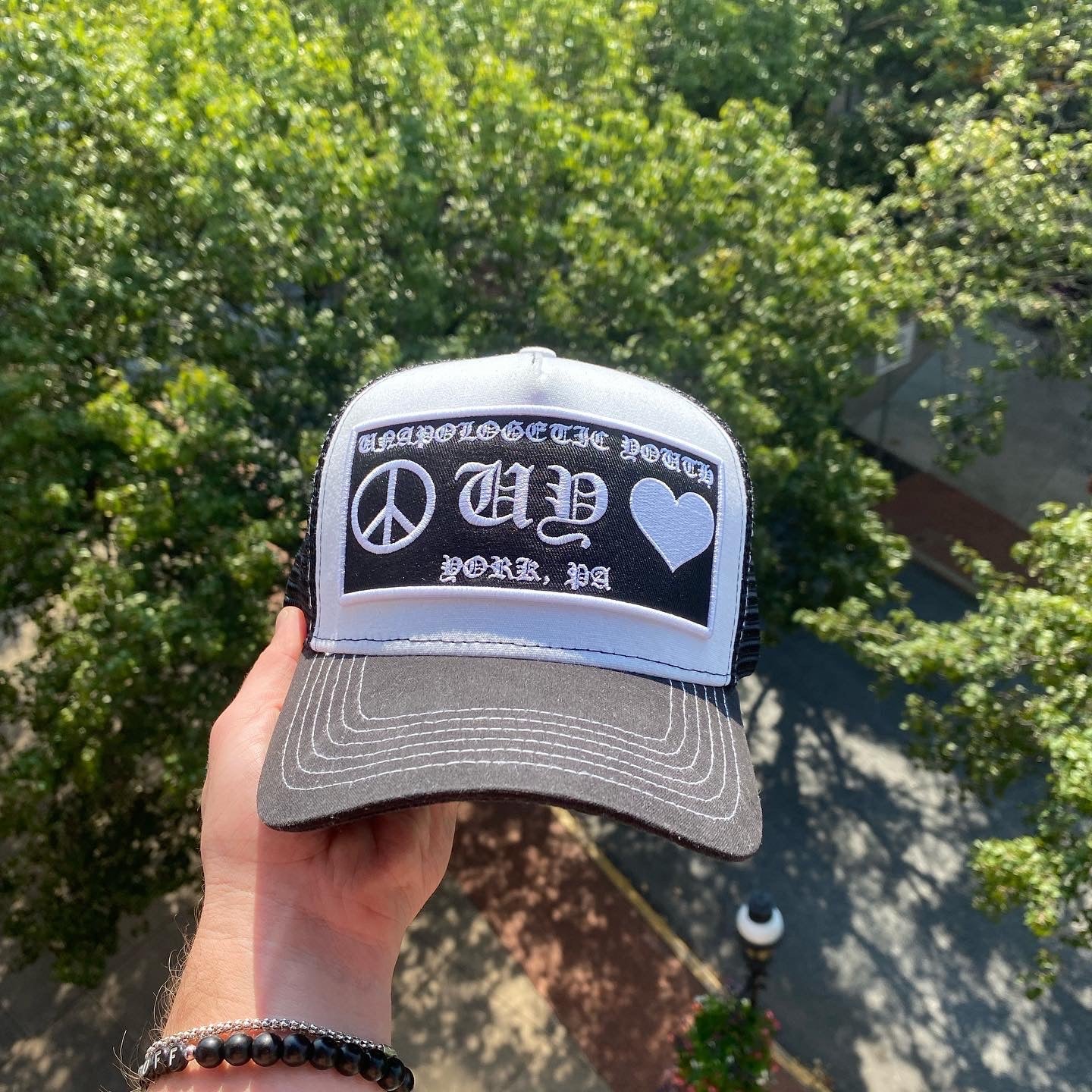 Unapologetic Youth Hearts trucker hat with a colorful heart graphic, adjustable mesh back, and curved brim.
